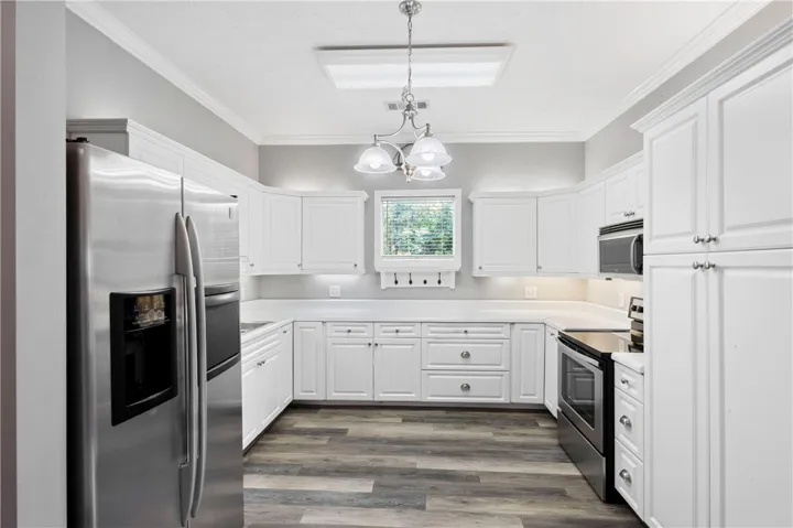 Bright white cabinetry and classic crown molding frame a well-appointed kitchen with durable wood-look flooring.
