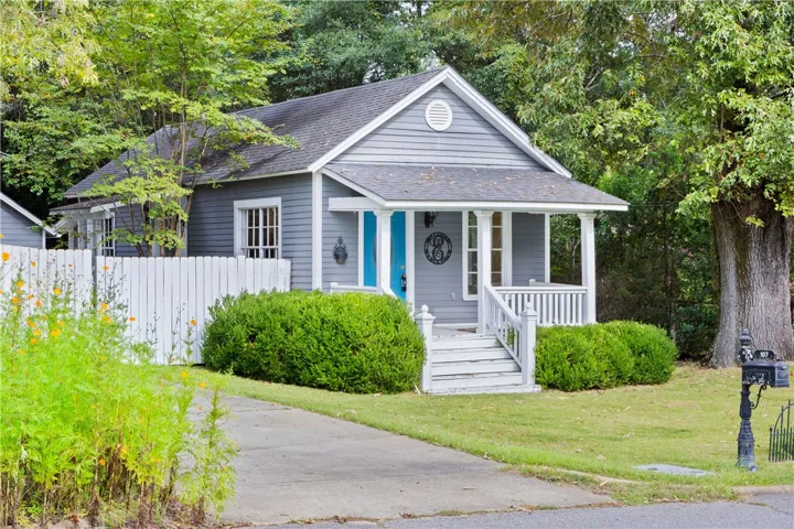 Mature trees frame a charming front porch overlooking the neat lawn and paved driveway.