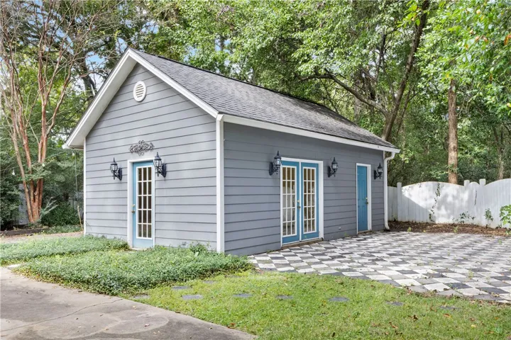 A charming detached outbuilding sits framed by mature trees and a patterned patio.