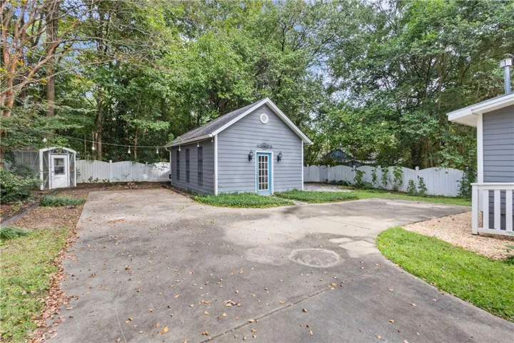 A detached outbuilding sits adjacent to a spacious concrete driveway surrounded by mature trees.