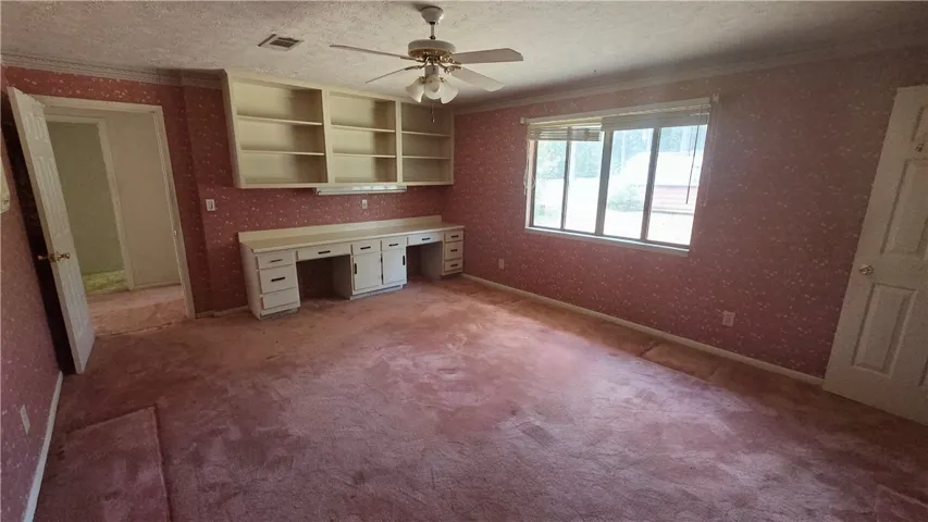 A spacious room features extensive built-in cabinetry, wide windows, and decorative crown molding.