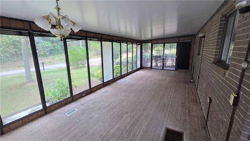 A wall of windows overlooks the surrounding greenery from this carpeted sunroom.
