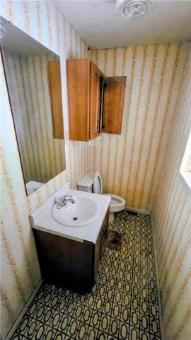 A compact half bath features patterned flooring, wallpapered walls, and functional cabinetry.