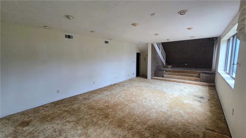 A spacious lower level recreation room features brick detailing and carpeted split-level stairs.