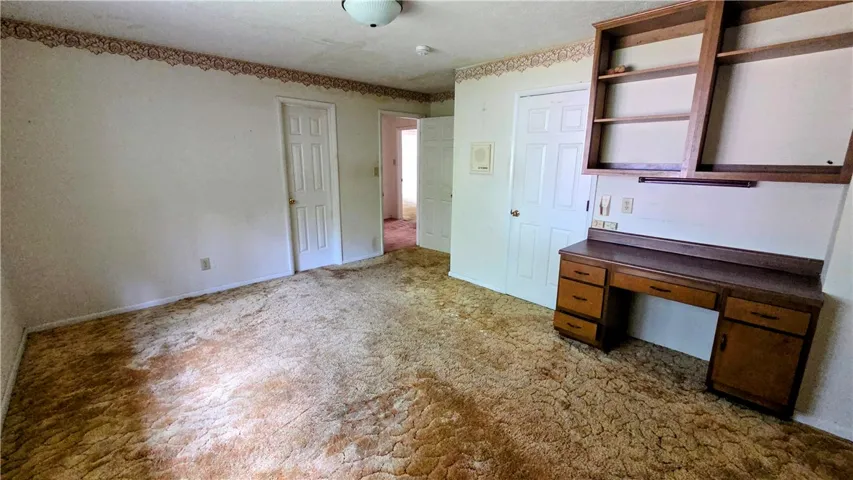 A spacious room features plush carpeting and a built-in desk with overhead wooden shelving.