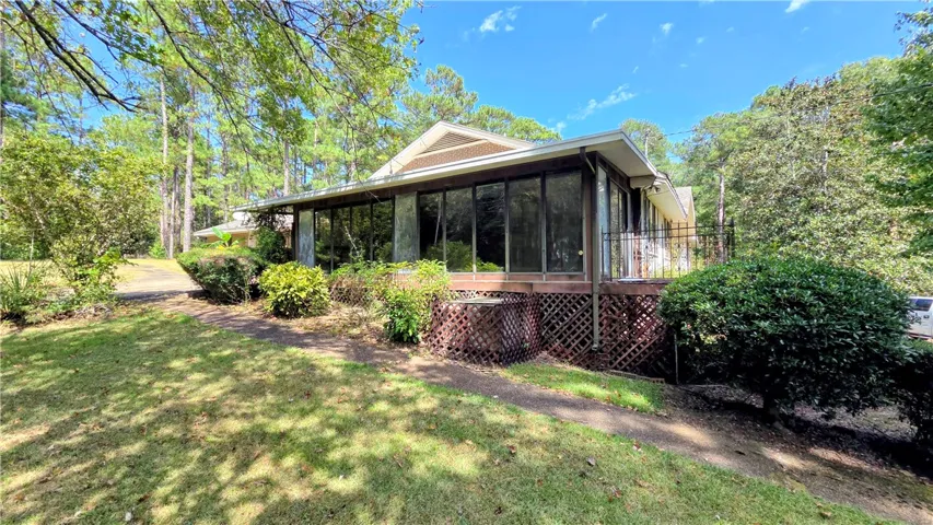 Mature trees frame a charming home featuring a large sunroom and lattice foundation detailing.