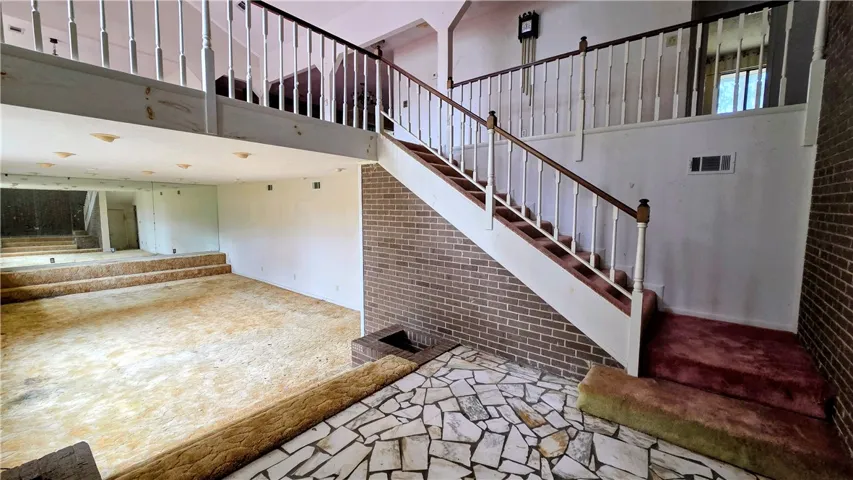 An open multi-level entryway features stone flooring, brick accents, and a dual-balcony landing overhead.