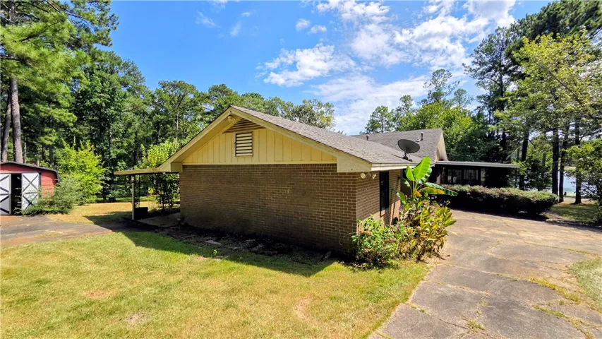 Mature trees frame a classic brick exterior with a paved driveway and detached storage building.