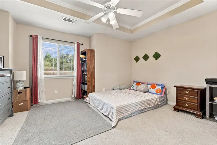 A tray ceiling and detailed crown molding elevate this carpeted bedroom space.