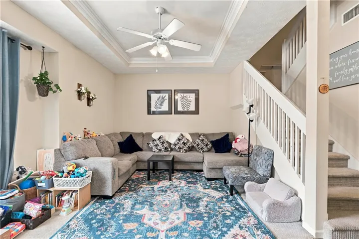 An inviting gathering space features a classic tray ceiling and adjacent carpeted staircase.