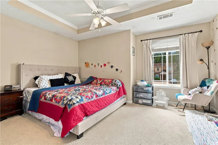 A classic tray ceiling and soft carpeted floors anchor this comfortable bedroom.