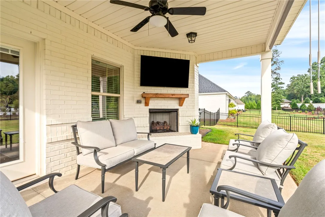 An inviting covered patio offers a masonry fireplace beneath structured ceilings and overlooks a green lawn.