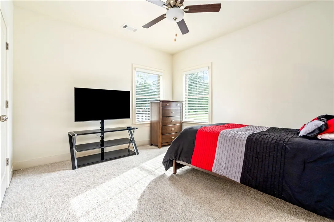 Natural light streams through multiple windows onto the soft carpeted flooring of this comfortable bedroom.
