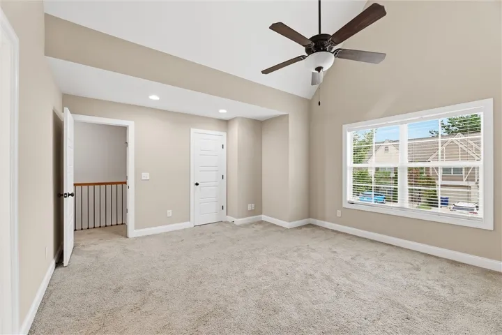 A vaulted ceiling and carpeted flooring define this light-filled upper-level bedroom.