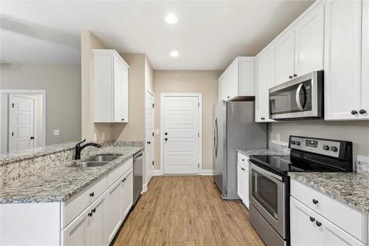 White cabinetry and stone countertops flank a central walkway of warm wood-textured flooring.