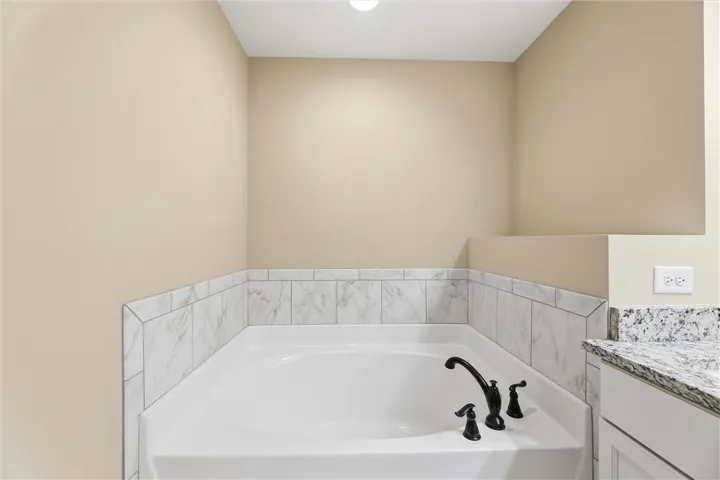 A deep soaking tub features elegant marble tile surround and dark hardware.