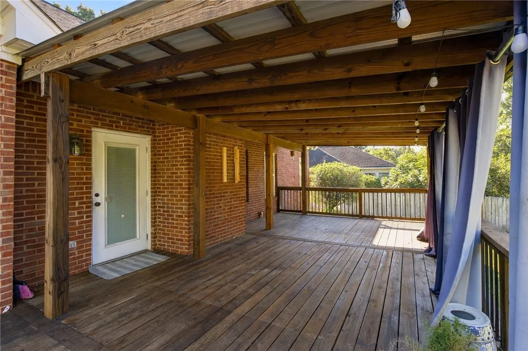 A spacious covered wooden deck features exposed overhead beams and rustic brick exterior accents.