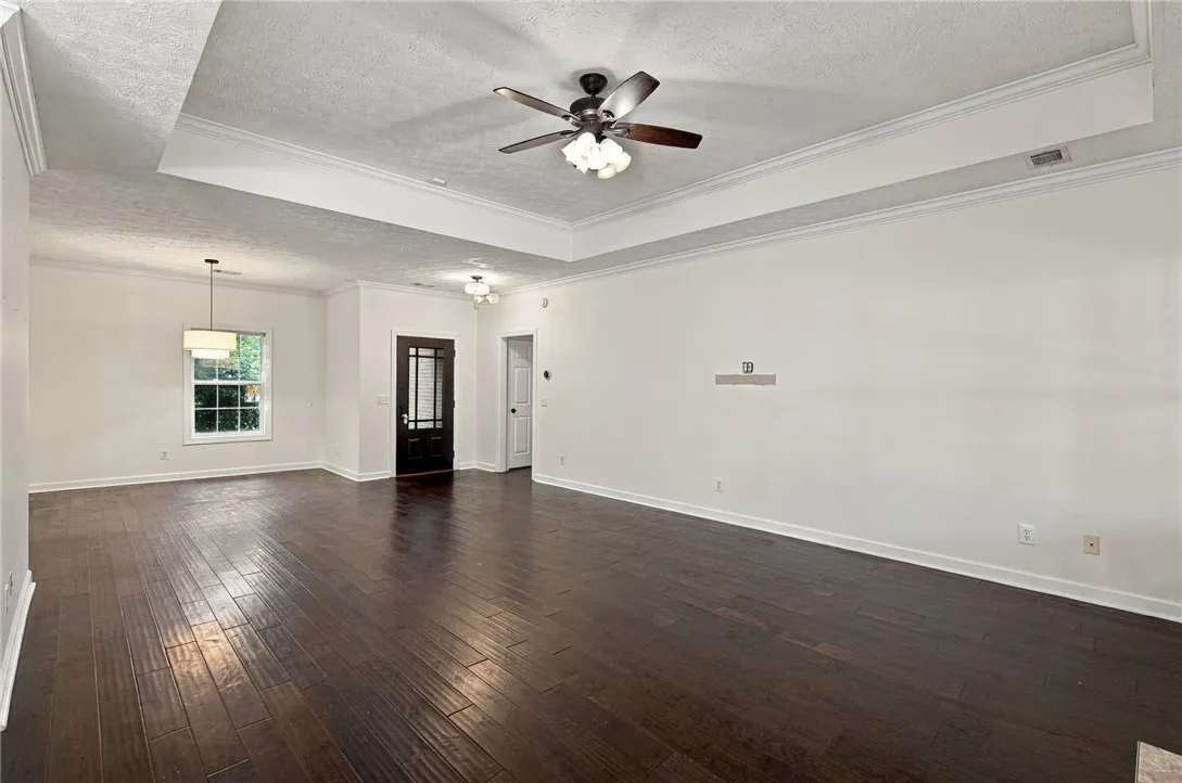 Rich hardwood flooring complements a detailed tray ceiling in this spacious, open-concept living area.