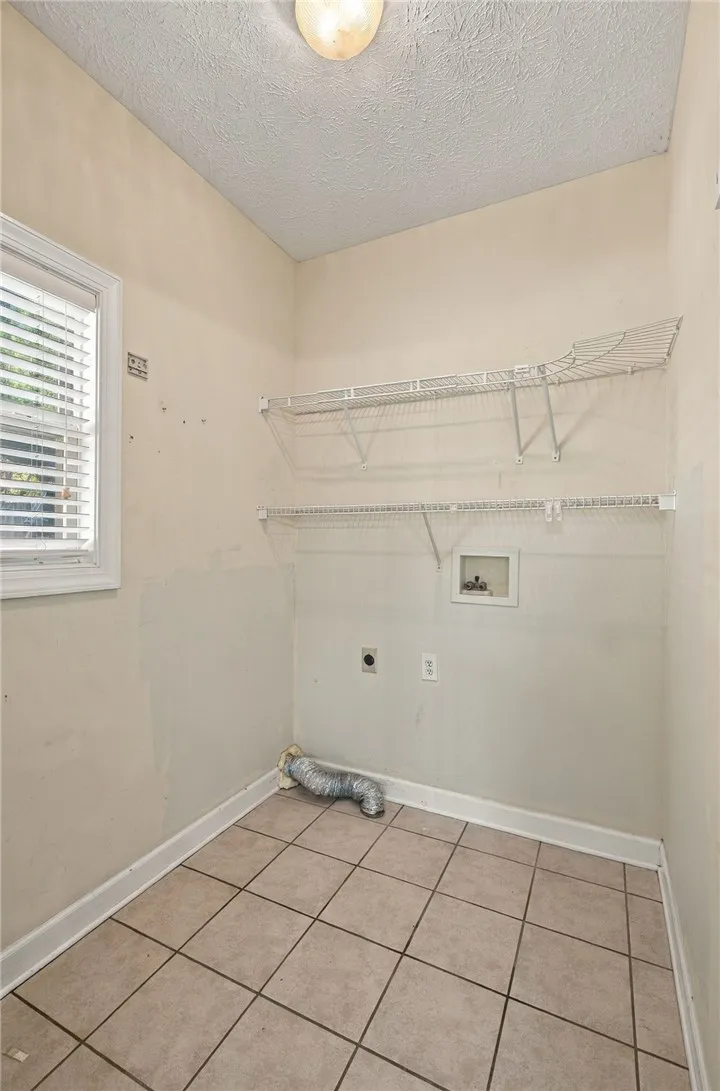 A dedicated laundry space features functional wire shelving, neutral tiled flooring, and a bright window.
