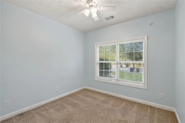 A spacious bedroom features neutral carpeting and a wide window overlooking the front yard.