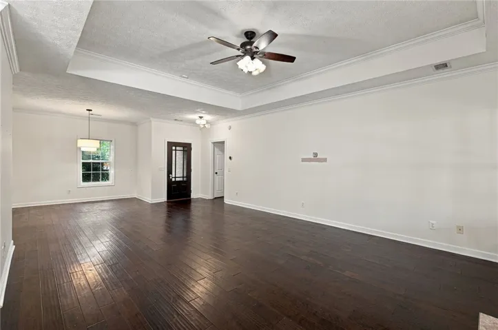 Rich hardwood flooring complements a detailed tray ceiling in this spacious, open-concept living area.