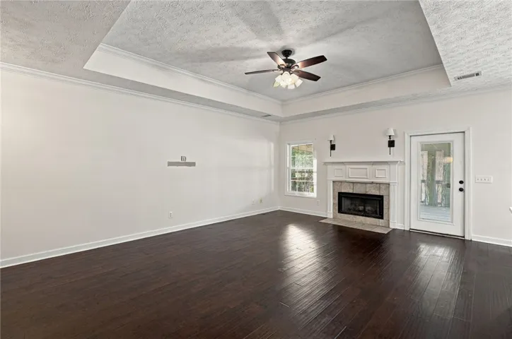 Rich hardwood flooring complements a classic fireplace and elegant tray ceiling in this spacious room.