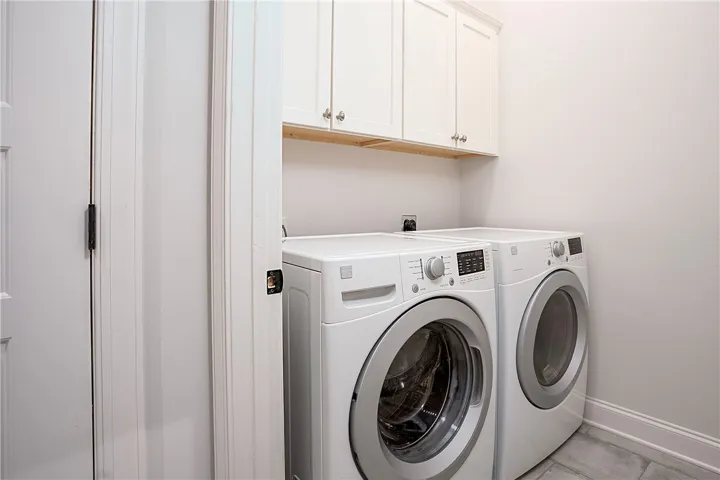 A dedicated laundry space features tile flooring and convenient overhead storage cabinetry.
