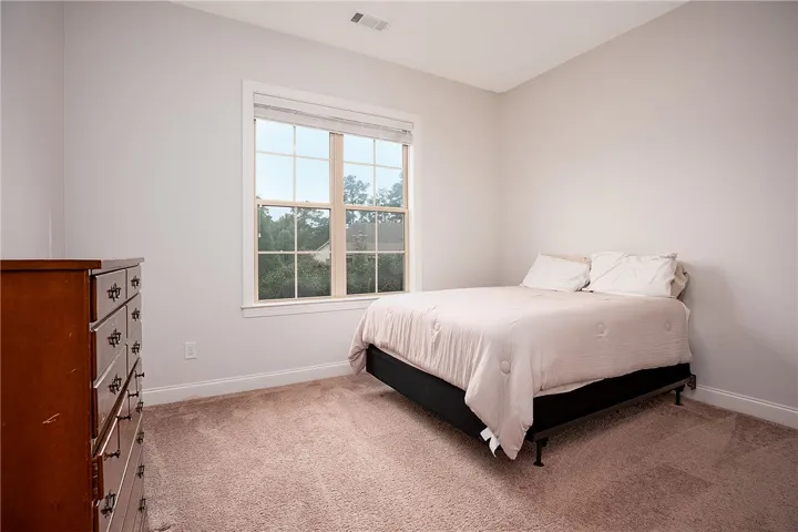Plush carpeting and a large window framing tree-lined views define this peaceful bedroom.