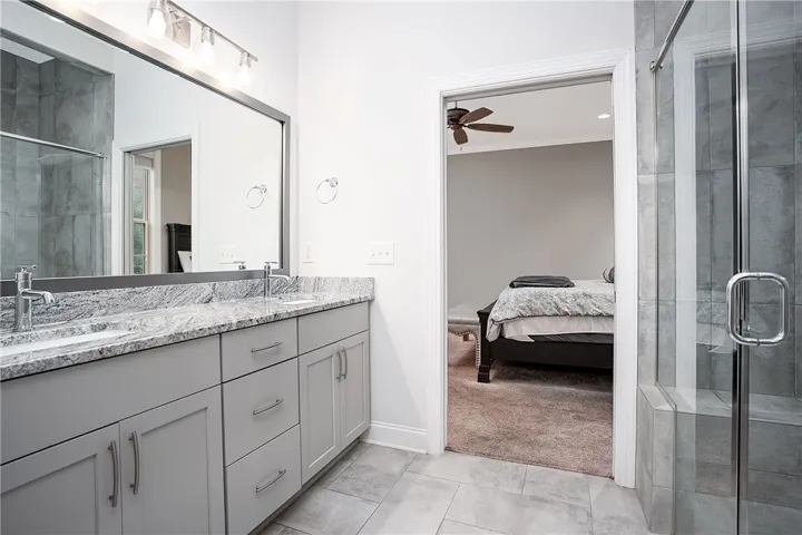 A spacious double vanity with granite countertops pairs perfectly with a glass-enclosed walk-in shower.
