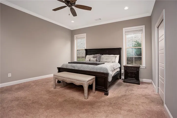 Crown molding frames the tall ceiling above plush carpeted flooring in this tranquil bedroom.