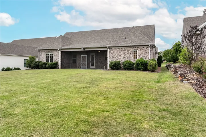 An expansive green lawn stretches behind a brick home featuring a screened rear porch.