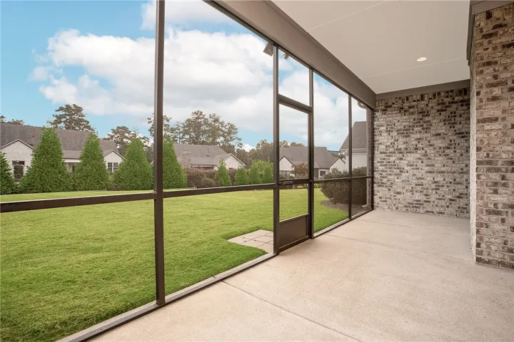 A screened porch with a brick accent wall overlooks a manicured grassy lawn.