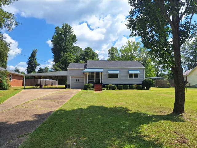 A classic ranch exterior with clean siding and a spacious paved driveway under mature shade trees.