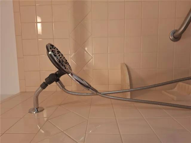 A tiled shower area includes integrated safety grab bars and a hand-held shower fixture.