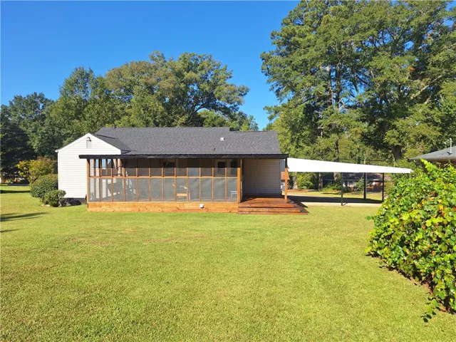 A spacious green lawn frames this classic home featuring a screened porch and attached carport.