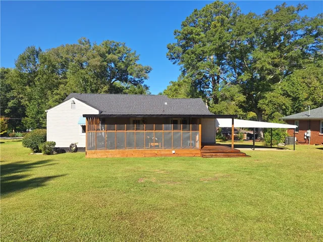 Mature trees frame the level grassy backyard and screened-in porch of this classic home.