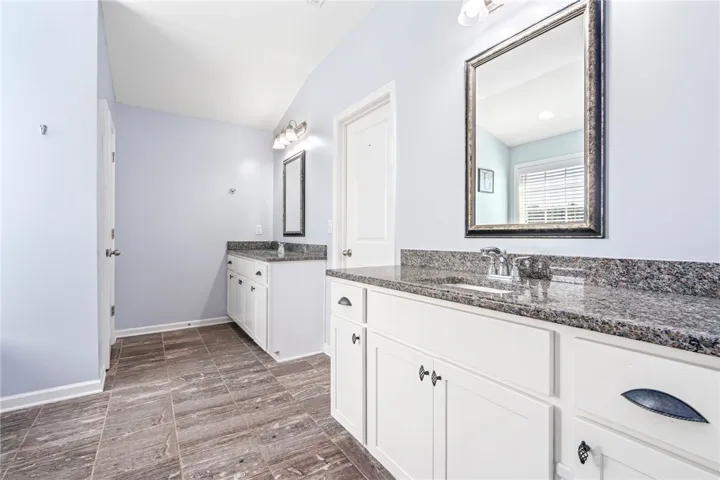 Dual white vanities with granite countertops flank a tile-floored path in this spacious bathroom.