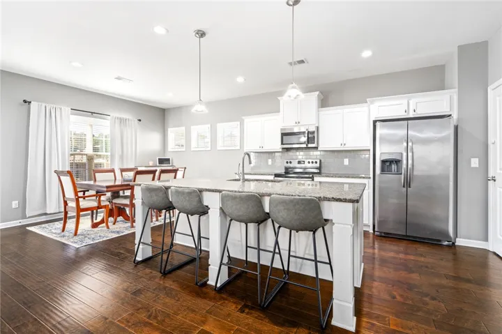 Rich hardwood floors anchor this open kitchen design complete with stone countertops and white cabinetry.