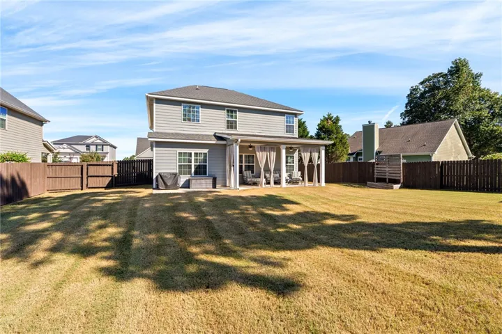 A sprawling green lawn complements the covered back patio and classic siding exterior.