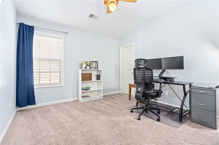A versatile home office features wall-to-wall carpeting and soft neutral wall finishes.