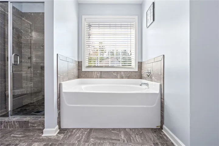 A deep soaking tub sits beneath a wide window next to a tiled glass shower.