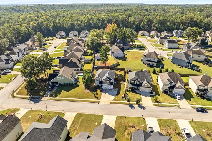 An aerial perspective captures a quiet suburban neighborhood surrounded by dense green forest.