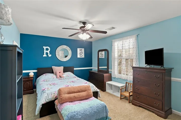 An inviting bedroom features plush carpeting and a bright window framed by classic chair rail molding.