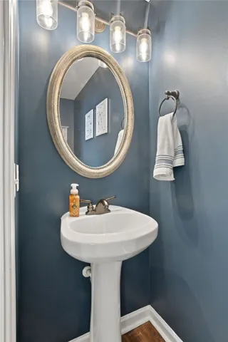 A classic pedestal sink sits beneath a custom oval mirror and warm vanity lighting.
