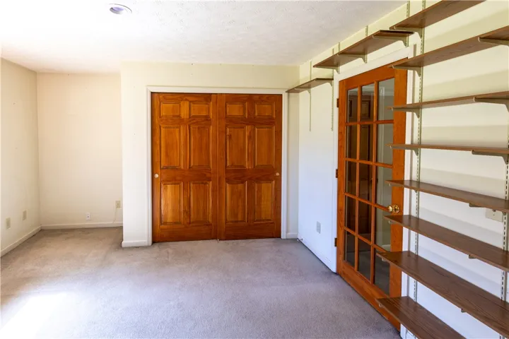 Warm wood doors and integrated wall shelving define this versatile carpeted room.