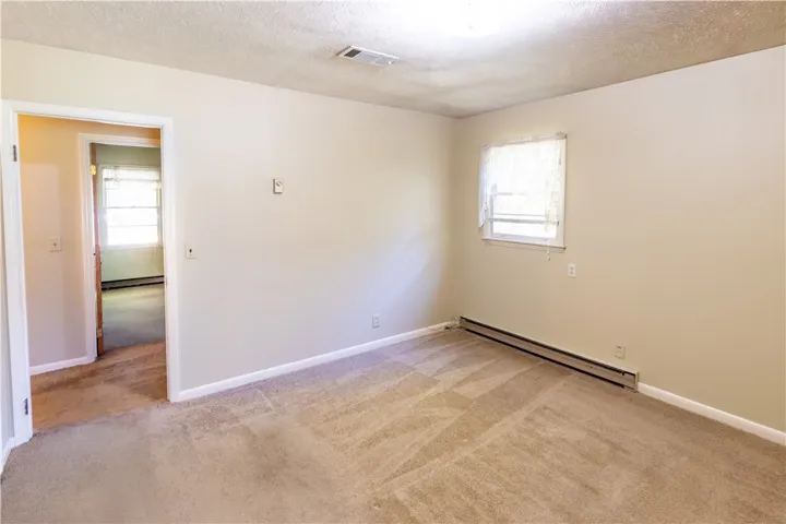 A window-lit bedroom features wall-to-wall carpeting and neutral trim leading to an adjacent hallway.
