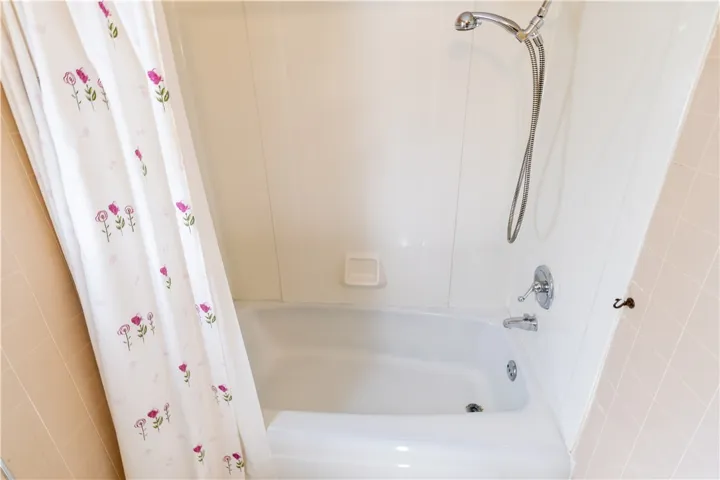Tiled walls flank a classic tub and shower combination with chrome fixtures.