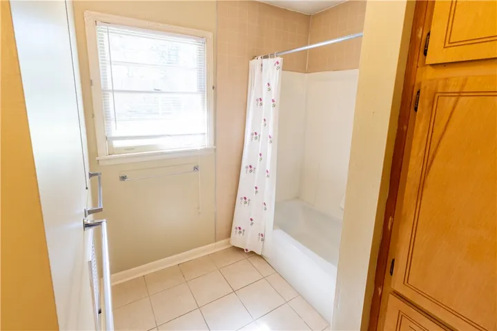 A classic tiled bathroom includes a tub and shower combination alongside wood cabinetry.