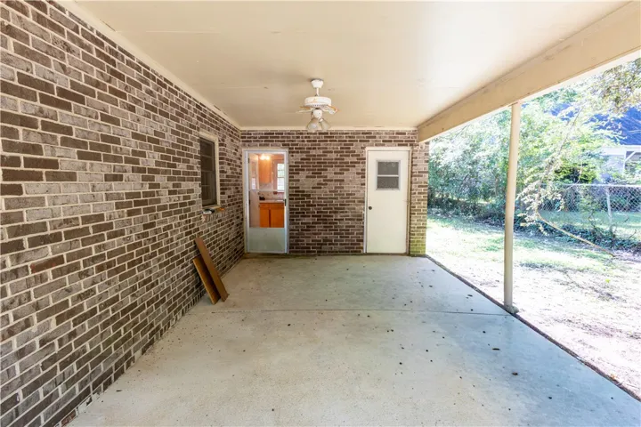 A covered concrete patio sits adjacent to a classic brick exterior, overlooking a grassy yard.