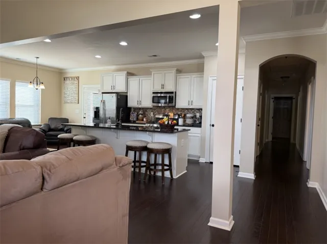 Rich dark wood flooring anchors the open kitchen and living area framed by elegant crown molding.